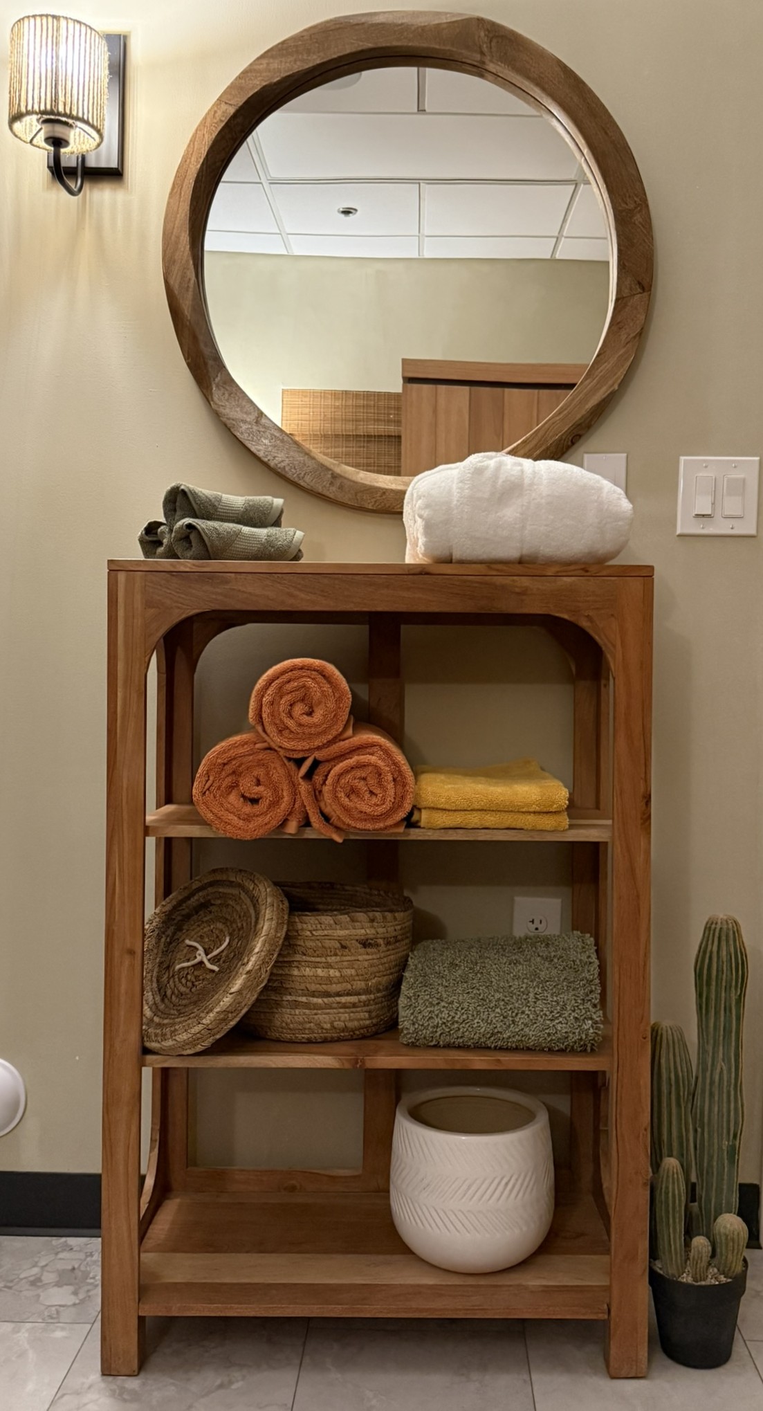 Bathroom console with folded towels, baskets, and a round wood-framed mirror